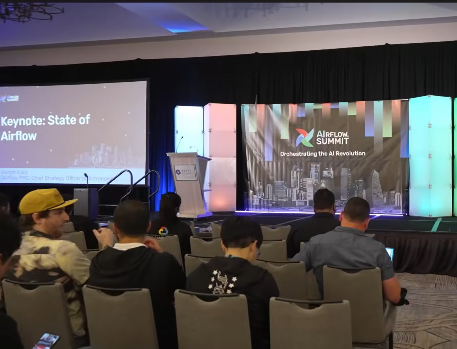Airflow Summit stage with the banner Orchestrating the AI Revolution and a screen showing Keynote: State of Airflow